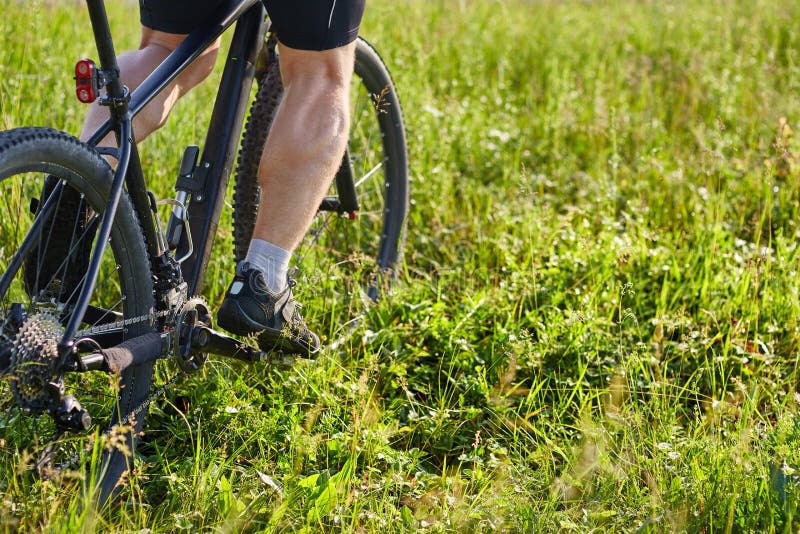 Zakończenie cyklisty mężczyzna iść na piechotę jeździeckiego rower górskiego na zielonej łące obraz royalty free Zakończenie cyklisty mężczyzna iść na piechotę jeździeckiego rower górskiego na zielonej łące obraz royalty free