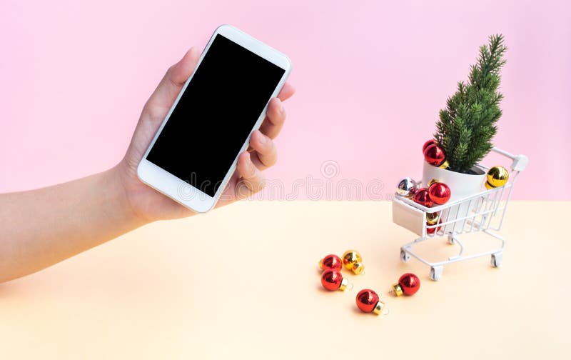 Zakupy online zimą, świąteczne koncepcje z młodą kobietą pokazującą smartfony i bożonarodzeniowe ozdoby w wózku bocznym, wózku zdjęcia royalty free Zakupy online zimą, świąteczne koncepcje z młodą kobietą pokazującą smartfony i bożonarodzeniowe ozdoby w wózku bocznym, wózku zdjęcia royalty free
