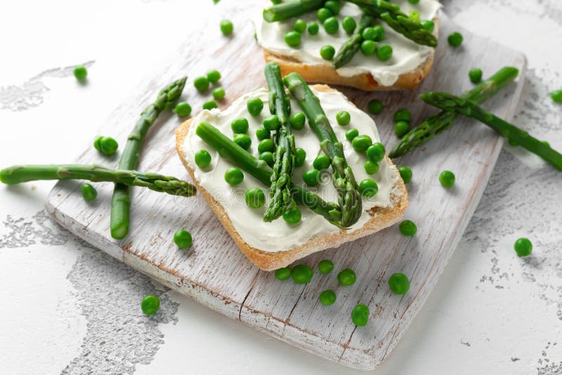 Zakąski bruschetta, grzanka z asparagusem, grochy i śmietankowy miękki ser, na białej desce obraz royalty free Zakąski bruschetta, grzanka z asparagusem, grochy i śmietankowy miękki ser, na białej desce obraz royalty free