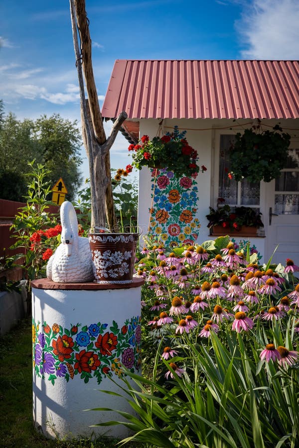 ZALIPIE, POLAND - August 1, 2021: A white well painted in colorful floral pattern, a bucket and a swan statue on top. Pink flowers in the garden. Sunny, summer day. ZALIPIE, POLAND - August 1, 2021: A white well painted in colorful floral pattern, a bucket and a swan statue on top. Pink flowers in the garden. Sunny, summer day.
