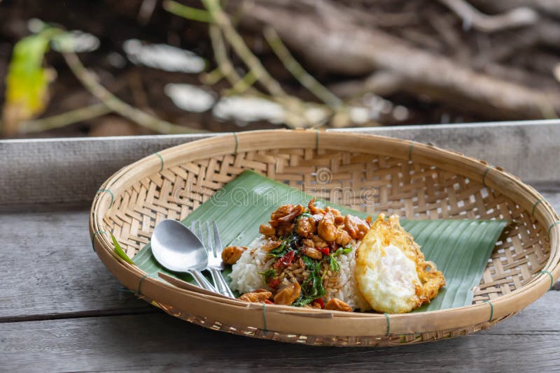Zamieszaj smażone liści bazylii Kurczak z ryżem i wkładaj smażone jaja do koszyka bambusowego na drewniany stół