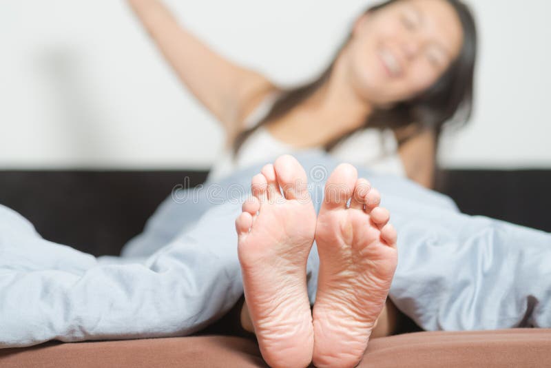 Close up of the cute crinkled soles of female feet belonging to a smiling playful woman relaxing in her bed with focus to the feet. Close up of the cute crinkled soles of female feet belonging to a smiling playful woman relaxing in her bed with focus to the feet