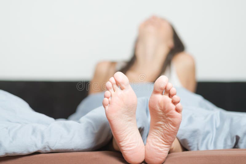 Close up of the cute crinkled soles of female feet belonging to a smiling playful woman relaxing in her bed with focus to the feet. Close up of the cute crinkled soles of female feet belonging to a smiling playful woman relaxing in her bed with focus to the feet