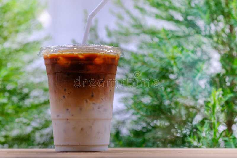 Zamyka w górę bierze oddaloną plastikową filiżankę lukrowy kawowy latte na drewnianym stole z zieloną naturą jako tło zdjęcie stock Zamyka w górę bierze oddaloną plastikową filiżankę lukrowy kawowy latte na drewnianym stole z zieloną naturą jako tło zdjęcie stock