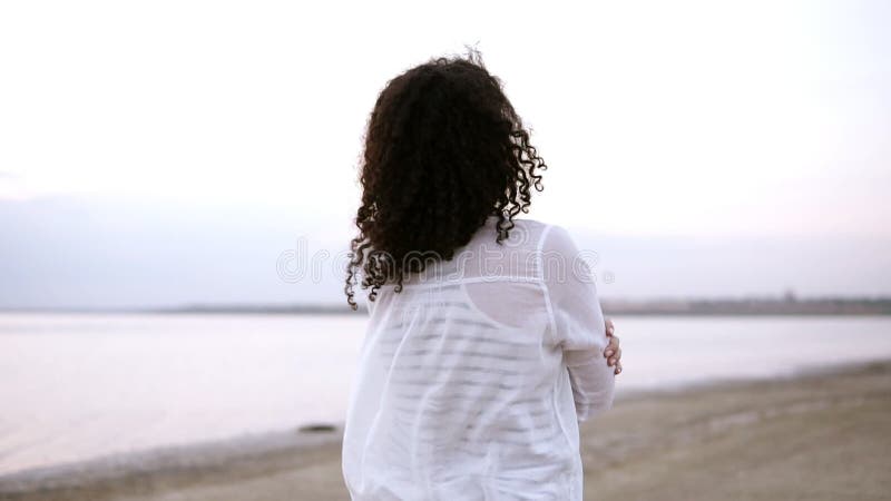 Zamyka w górę bocznego materiału filmowego atrakcyjny młodej kobiety odprowadzenie nadmorski w wodzie, jest ubranym białą koszula