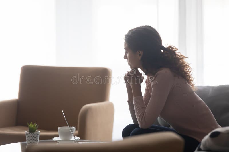 Thoughtful young woman sit on sofa at home distracted form computer work suffering from work or life problems, pensive Caucasian female look in distance thinking or pondering, dilemma concept. Thoughtful young woman sit on sofa at home distracted form computer work suffering from work or life problems, pensive Caucasian female look in distance thinking or pondering, dilemma concept