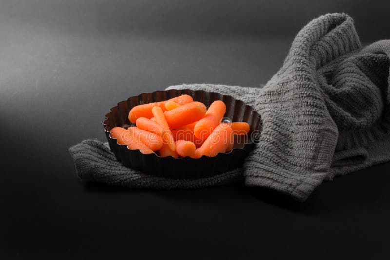 Zanahorias de bebé en plato de la hornada y toalla gris con el fondo oscuro foto de archivo libre de regalías Zanahorias de bebé en plato de la hornada y toalla gris con el fondo oscuro foto de archivo libre de regalías