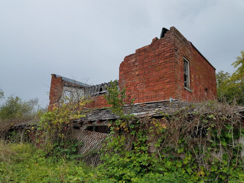 Abandoned brick asylum outbuilding in a field with overgrown grass and ivy and a wooden fence leaning at an angle. Abandoned brick asylum outbuilding in a field with overgrown grass and ivy and a wooden fence leaning at an angle.