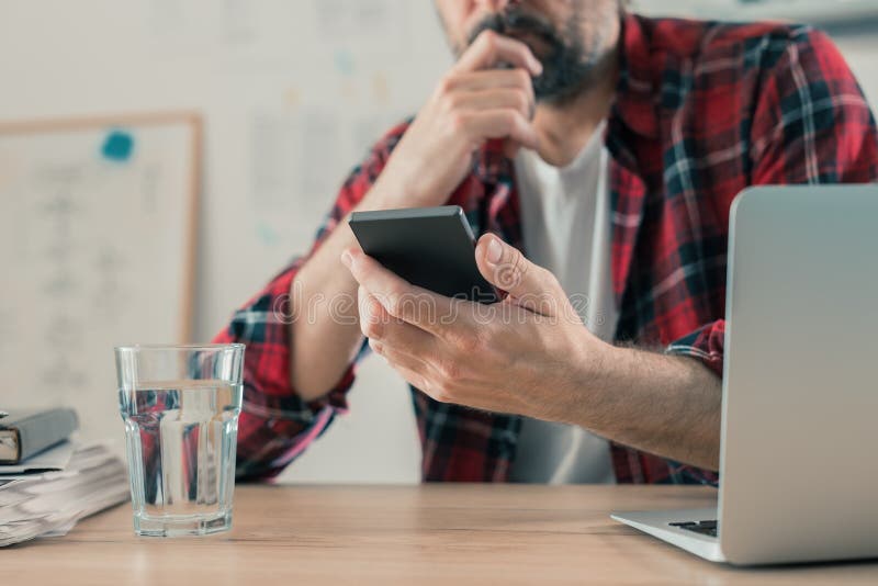 Concerned freelancer reading text message on mobile phone in his small business home office, selective focus. Concerned freelancer reading text message on mobile phone in his small business home office, selective focus