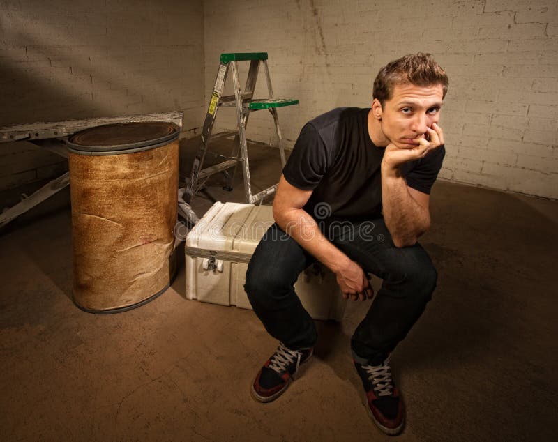 Bored laborer sitting on cooler in unfinished basement. Bored laborer sitting on cooler in unfinished basement