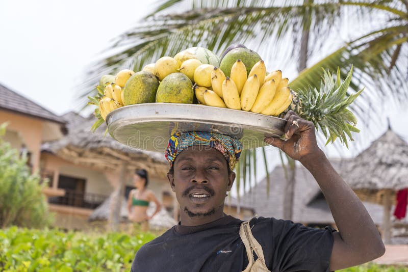 Zanzibar, Tanzania - january 15, 2020 : African man holds fresh tropical fruits for sale for tourist on the head near beach of Zanzibar island, Tanzania, East Africa, close up