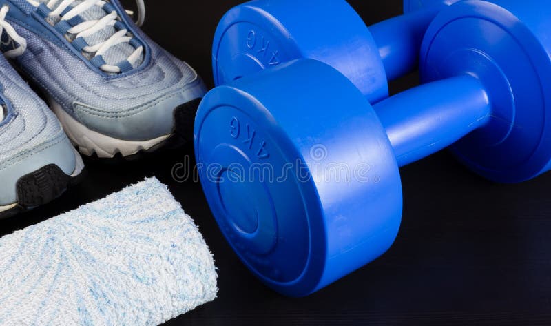 Zapatillas de deporte, pesas de gimnasia y una toalla en un fondo oscuro imágenes de archivo libres de regalías Zapatillas de deporte, pesas de gimnasia y una toalla en un fondo oscuro imágenes de archivo libres de regalías