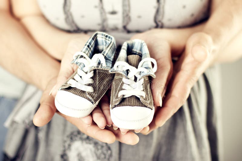 Zapatillas de deporte recién nacidas del bebé en las manos de la familia, padres que llevan a cabo botines recién nacidos de los fotos de archivo libres de regalías Zapatillas de deporte recién nacidas del bebé en las manos de la familia, padres que llevan a cabo botines recién nacidos de los fotos de archivo libres de regalías