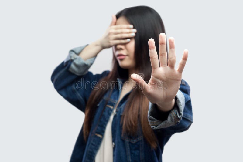 Stop, I dob`t want to see this. Portrait of scared brunette young woman in casual blue denim jacket standing closed eyes and showing stop gesture. indoor studio shot, isolated on light grey background. Stop, I dob`t want to see this. Portrait of scared brunette young woman in casual blue denim jacket standing closed eyes and showing stop gesture. indoor studio shot, isolated on light grey background