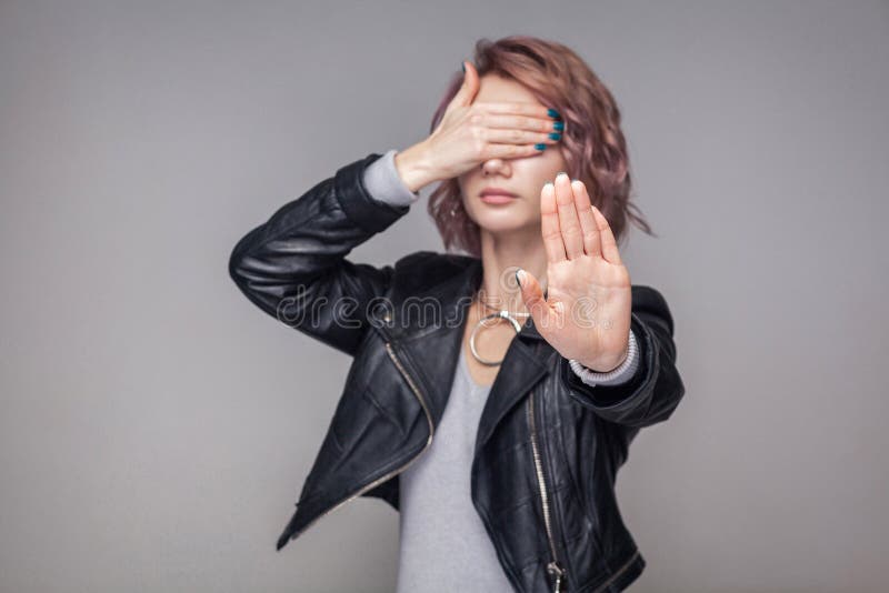 Stop, I dont want to see. Portrait of blocking girl with short hairstyle and makeup in casual style black leather jacket standing with stop gesture. indoor studio shot, isolated on grey background. Stop, I dont want to see. Portrait of blocking girl with short hairstyle and makeup in casual style black leather jacket standing with stop gesture. indoor studio shot, isolated on grey background