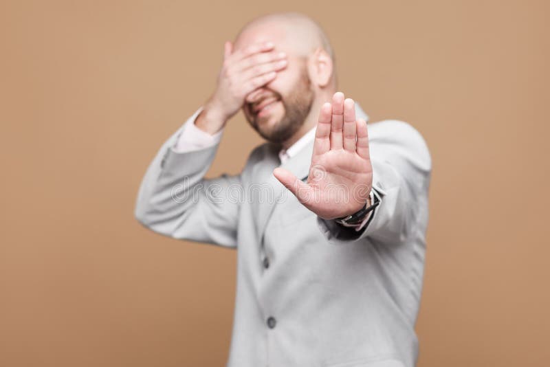 Stop it, I dont want to see it. Portrait of confused middle aged bald bearded businessman in classic light gray suit standing with stop gesture, covered his eyes. studio shot on brown background. Stop it, I dont want to see it. Portrait of confused middle aged bald bearded businessman in classic light gray suit standing with stop gesture, covered his eyes. studio shot on brown background.