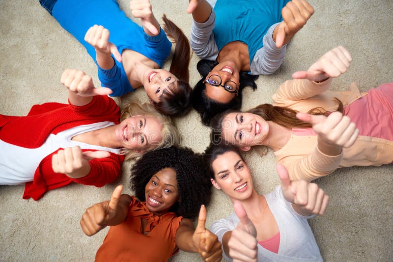 Diversity, race, ethnicity and people concept - international group of happy smiling different women lying on floor in circle and showing thumbs up. Diversity, race, ethnicity and people concept - international group of happy smiling different women lying on floor in circle and showing thumbs up