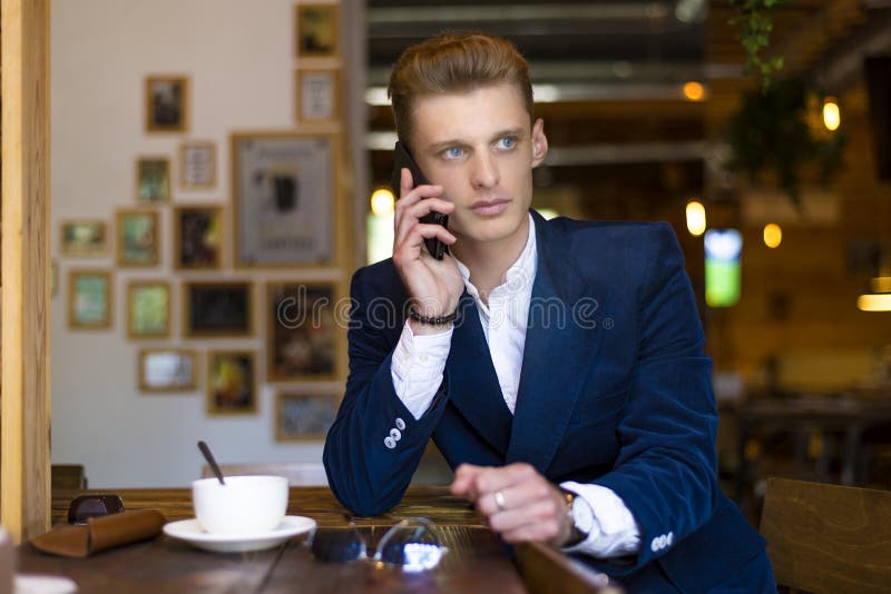 Zbliżenie portret poważny przystojny mężczyzna opowiada na smartphone i obsiadaniu przy stołem w kawiarni Frontowy widok obraz stock Zbliżenie portret poważny przystojny mężczyzna opowiada na smartphone i obsiadaniu przy stołem w kawiarni Frontowy widok obraz stock