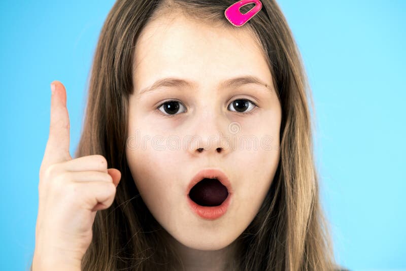 Close up portrait of a child school girl holding up point finger in I have an idea gesture isolated on blue background. Close up portrait of a child school girl holding up point finger in I have an idea gesture isolated on blue background.