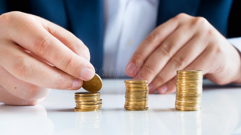 Zbliżenie wizerunek stawia złote monety w wysokości stertach na biurowym biurku męski bankowiec obrazy stock Zbliżenie wizerunek stawia złote monety w wysokości stertach na biurowym biurku męski bankowiec obrazy stock