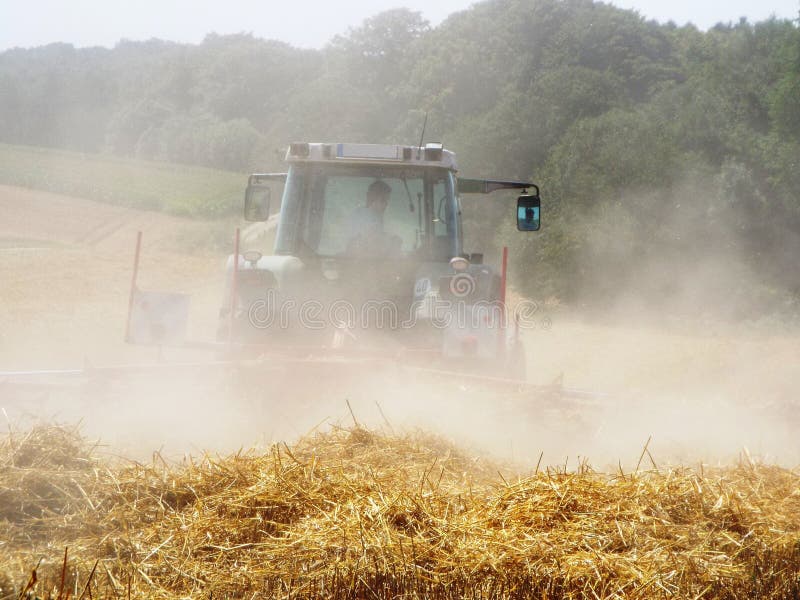 A straw turner in action: When turning the straw the turner swirls on a cloud of dust. Germany 02.08.2015. A straw turner in action: When turning the straw the turner swirls on a cloud of dust. Germany 02.08.2015