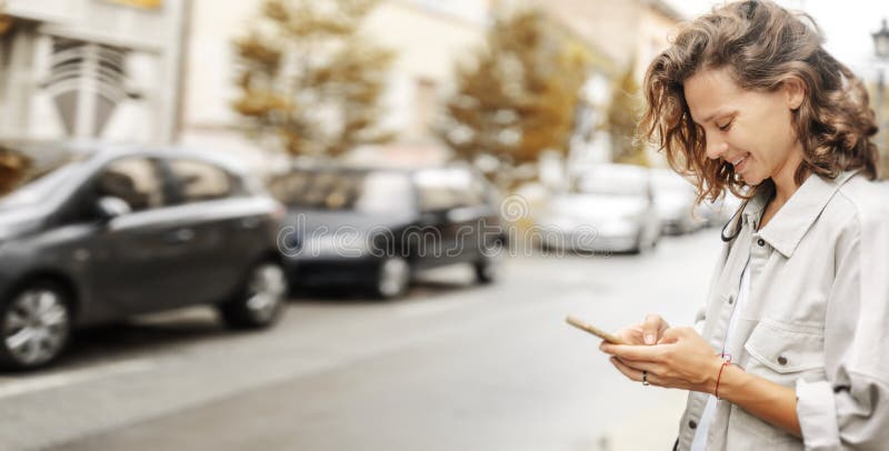 Zdjęcie radosnej, szczęśliwej kobiety uśmiechającej się i używającej telefonu komórkowego podczas spaceru na ulicy miasta obraz royalty free