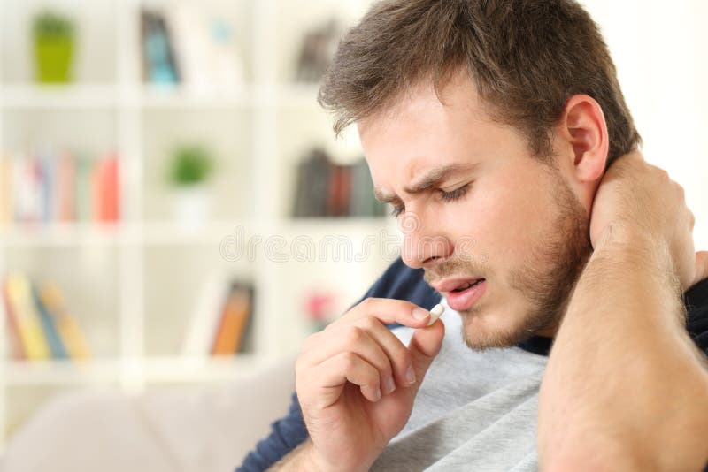 Injured man complaining taking a pill sitting on a couch in the living room in a house interior. Injured man complaining taking a pill sitting on a couch in the living room in a house interior