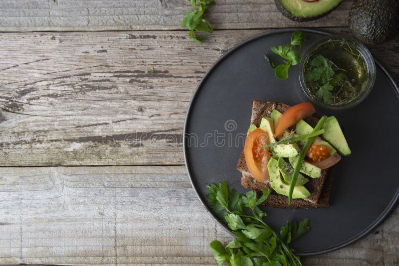 Zdrowa avocado kanapka na ciemnym żyto grzanki chlebie robić z świeżym pokrojonym avocado, ziarnami i pomidorami, na nieociosanym obraz stock Zdrowa avocado kanapka na ciemnym żyto grzanki chlebie robić z świeżym pokrojonym avocado, ziarnami i pomidorami, na nieociosanym obraz stock
