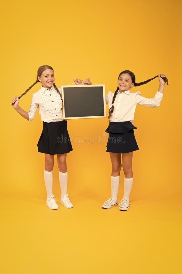 Healthier hair from root to tip. Cute small children with plaited hair holding blackboard on yellow background. Happy little girls with long hair braids and chalkboard. Braiding hair for school. Healthier hair from root to tip. Cute small children with plaited hair holding blackboard on yellow background. Happy little girls with long hair braids and chalkboard. Braiding hair for school.
