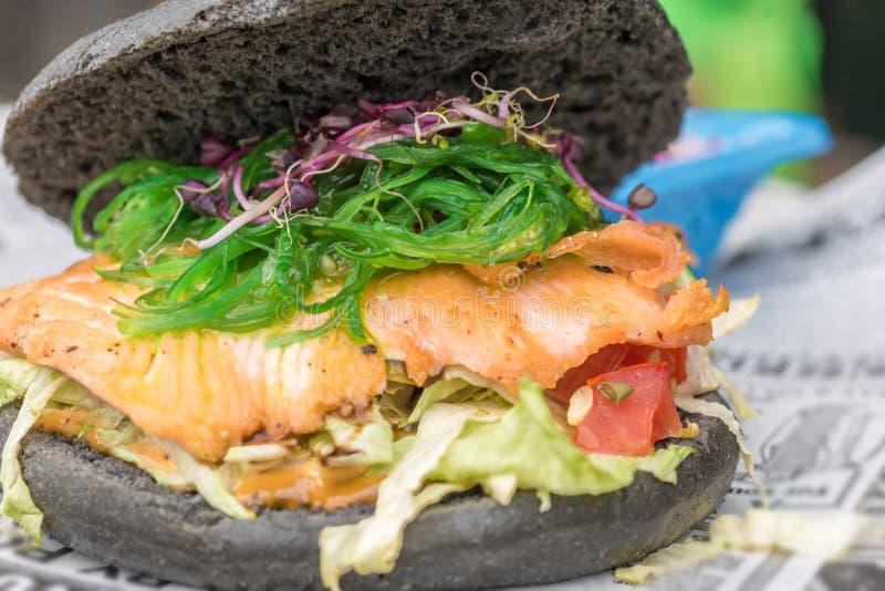Zdrowy czarny hamburger z rybią i świeżą sałatką jako smakowita przekąska obraz royalty free Zdrowy czarny hamburger z rybią i świeżą sałatką jako smakowita przekąska obraz royalty free