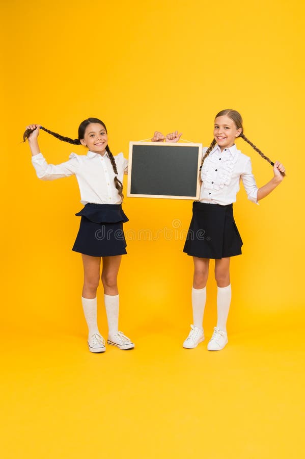 Healthier hair from root to tip. Cute small children with plaited hair holding blackboard on yellow background. Happy little girls with long hair braids and chalkboard. Braiding hair for school. Healthier hair from root to tip. Cute small children with plaited hair holding blackboard on yellow background. Happy little girls with long hair braids and chalkboard. Braiding hair for school.