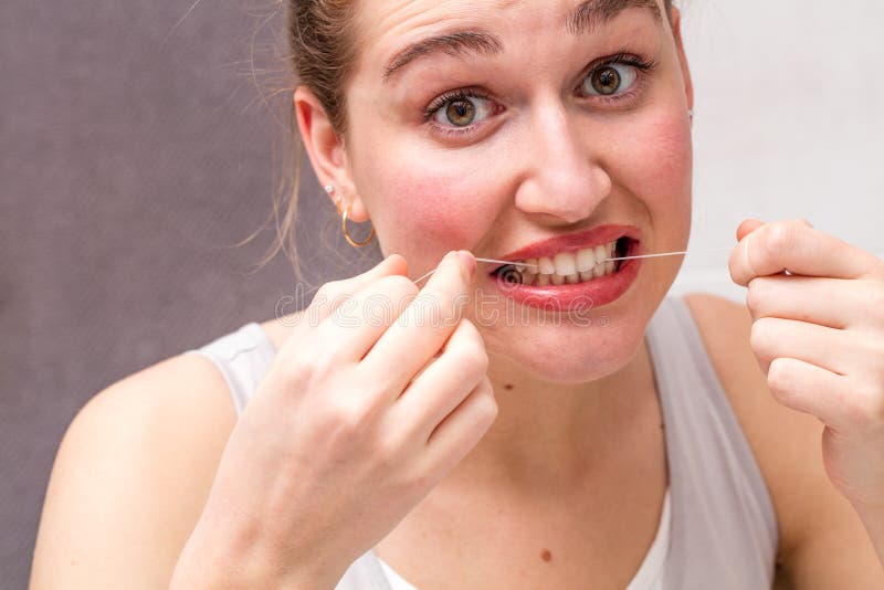 Zdziwiona młoda kobieta mleje jej zęby w używać stomatologicznego floss obraz stock Zdziwiona młoda kobieta mleje jej zęby w używać stomatologicznego floss obraz stock