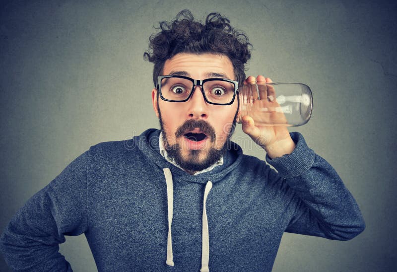 Funny surprised man in glasses holding glass jar next to ear and listening to secrets. Funny surprised man in glasses holding glass jar next to ear and listening to secrets.