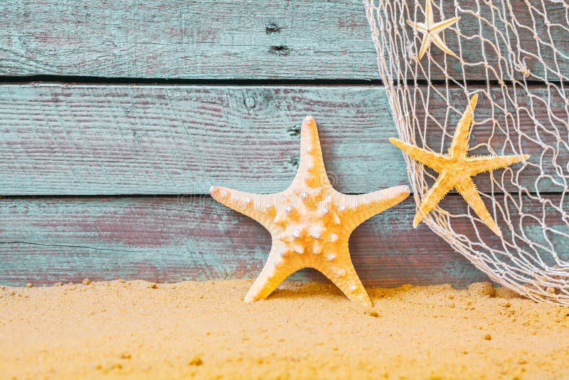 Nautical background with starfish and a fishing net against rustic weathered blue wooden planks above golden beach sand. Nautical background with starfish and a fishing net against rustic weathered blue wooden planks above golden beach sand