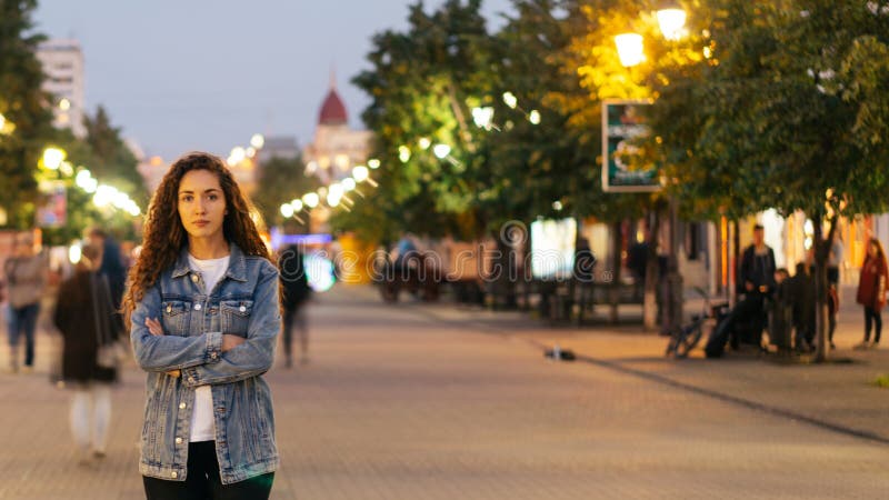 Zeit-Versehen des unglücklichen Mädchens allein spät stehend auf schöner Fußgängerstraße am Abend und Kamera betrachtend wenn