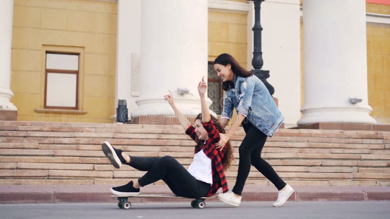 Zeitlupe von den aufgeregten Mädchen, die mit dem Skateboard sitzt auf longboard und drückt sie Spaß lachend und habend spielen