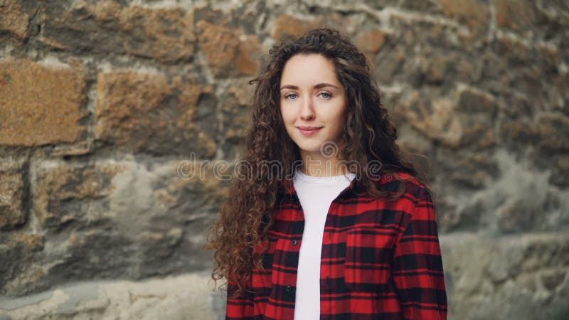 Zeitlupeporträt der lächelnden jungen Frau mit langem gelocktes Haar tragendem weißem T-Shirt und heller Hemdstellung