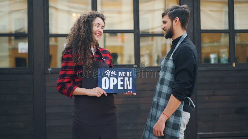 Zeitlupeporträt von zwei glücklichen Unternehmercaféinhabern, die mit offenem Zeichen vor dem Neubau sich wendet an aufwerfen