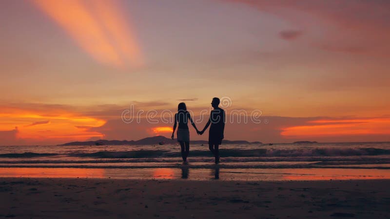 Zeitlupeschattenbild von glücklichen liebevollen Paaren gehen am Strand auf Sonnenuntergang im Ozeanufer