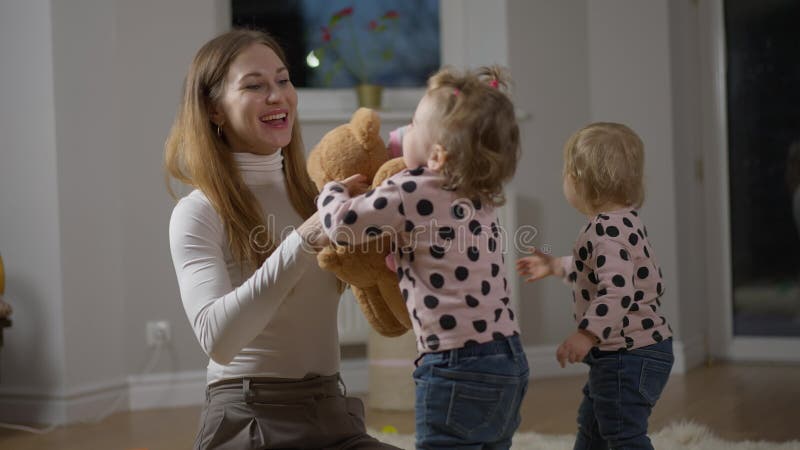 Zelfverzekerde kaukasische vrouw zingt langzaam dansend met tweelingdochters binnen. gelukkig