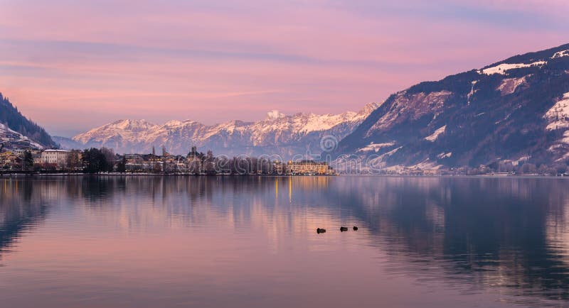 Zell am See in winter evening. View of Lake Zell, town, mountains and snow with reflections in water. Alpine town at