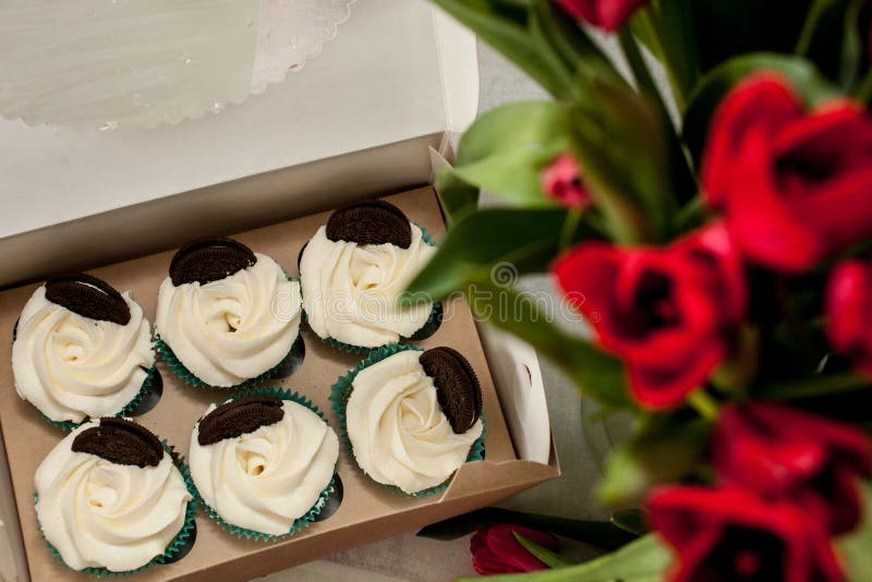 Zes cupcakes met witte die kaasroom met koekjes in een doos en een vaag boeket van tulpen hoogste mening wordt verfraaid royalty-vrije stock foto Zes cupcakes met witte die kaasroom met koekjes in een doos en een vaag boeket van tulpen hoogste mening wordt verfraaid royalty-vrije stock foto
