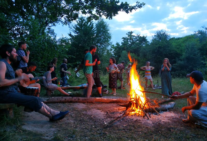 Zhytomyr, Ukraine - June 15, 2018: Happy people play guitar and drums around campfire in forest. Musical jam, freedom concept, social leisure. Zhytomyr, Ukraine - June 15, 2018: Happy people play guitar and drums around campfire in forest. Musical jam, freedom concept, social leisure