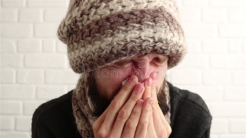 Zieke man in brei-hoed die zijn neus blaast en zich koud dicht voelt