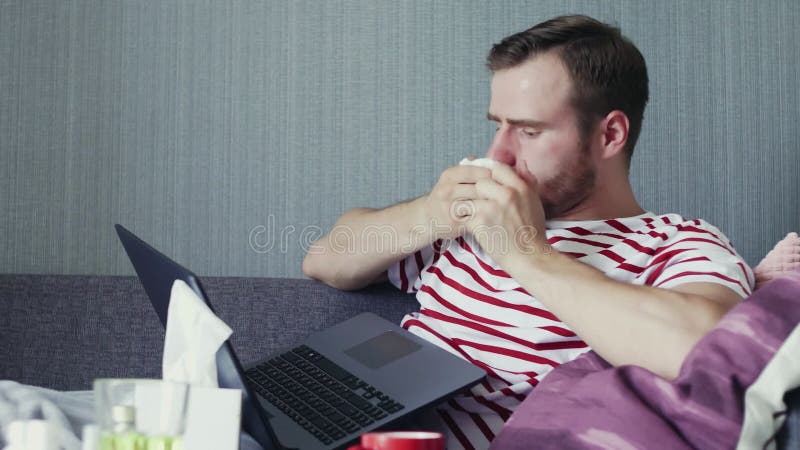 Zieke man die een laptop gebruikt en een neus blaast met zakdoek