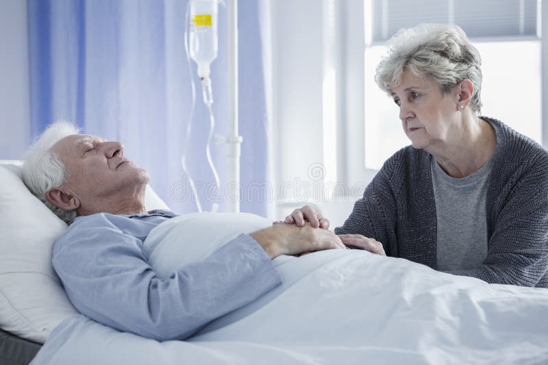 Worried wife taking care of sick men lying connected to a drip. Worried wife taking care of sick men lying connected to a drip