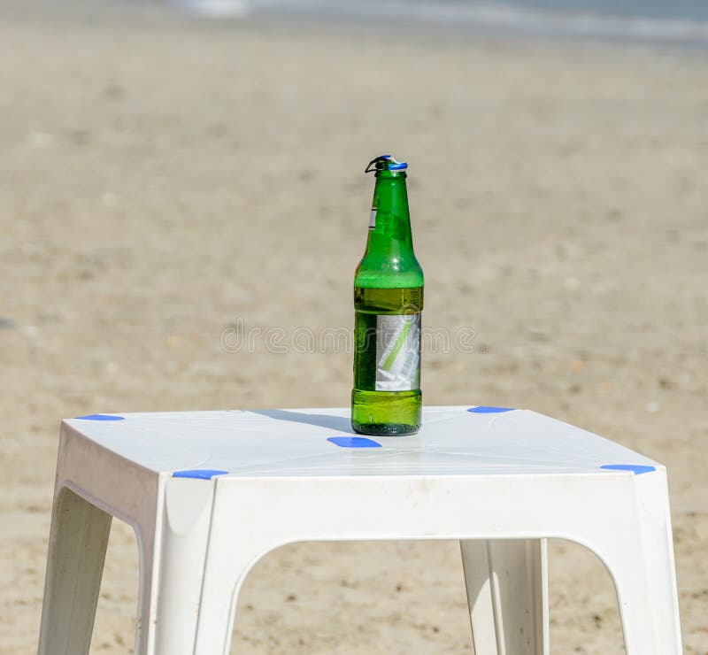 Zielona butelka piwna pozycja na białym plaża stole, zamyka up fotografia royalty free