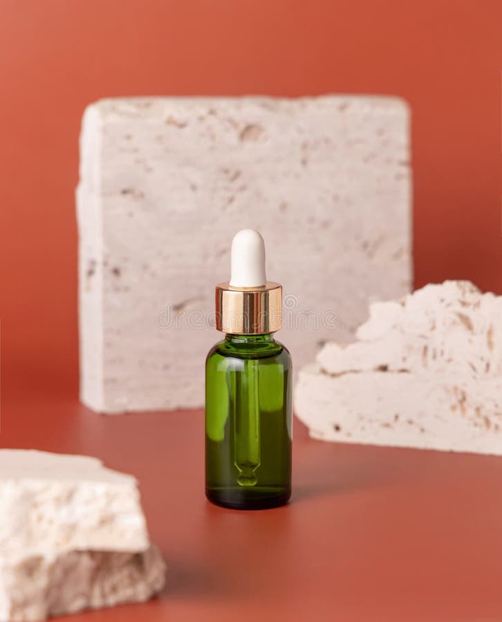 Green dropped bottle near travertine stones on pink close up, cosmetic mockup. Skincare beauty product. Natural cosmetics. Minimal composition. Green dropped bottle near travertine stones on pink close up, cosmetic mockup. Skincare beauty product. Natural cosmetics. Minimal composition