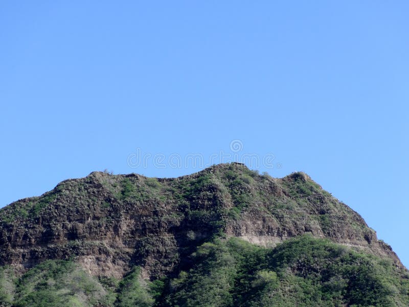 Green crater rim of Diamond Head, a volcanic tuff cone on the island of Oʻahu, Hawaii. The crater is a natural wonder that was formed by a volcanic eruption about 300,000 years ago. The crater is now a state monument and a popular hiking destination. The photo was taken from a distance, so the crater appears small in the frame, but it is actually 3,520 feet in diameter and 761 feet in height. The. Green crater rim of Diamond Head, a volcanic tuff cone on the island of Oʻahu, Hawaii. The crater is a natural wonder that was formed by a volcanic eruption about 300,000 years ago. The crater is now a state monument and a popular hiking destination. The photo was taken from a distance, so the crater appears small in the frame, but it is actually 3,520 feet in diameter and 761 feet in height. The