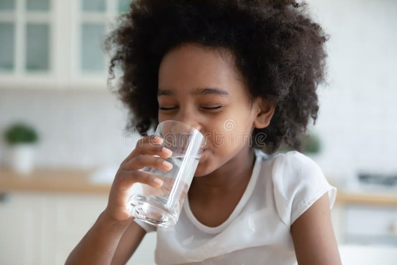 Ziemlich wenig Afroamerikanermädchen, das Süßwasser in der Küche trinkt lizenzfreies stockfoto